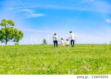 青空の草原を手を繫いで歩く家族 139076044