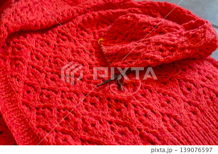 Beautiful cotton knitting pattern. Knitted fashion. Bright orange knitted cardigan with wooden needles. Handmade knitted sweater. Knitting hobby concept. Red summer clothing. Beautiful cotton knitting pattern. Knitted fashion. Bright orange knitted cardigan with wooden needles. Handmade knitted sweater. Knitting hobby concept. Red summer clothing. 139076597