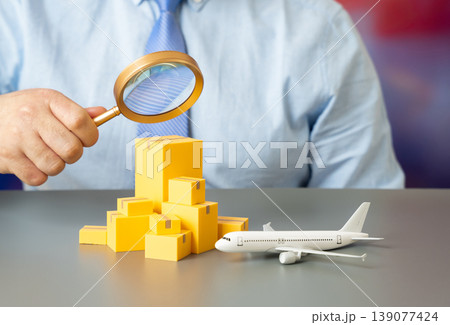 A man examines goods near an airplane through a magnifying glass. Air freight concept highlights inspection. Logistics, security and global trade rely on efficient cargo transport. A man examines goods near an airplane through a magnifying glass. Air freight concept highlights inspection. Logistics, security and global trade rely on efficient cargo transport. 139077424