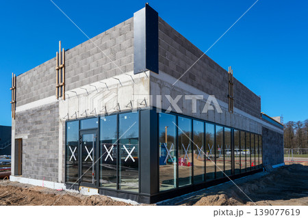 Modern commercial building with glass facade and concrete walls under construction in sunlight Modern commercial building with glass facade and concrete walls under construction in sunlight 139077619