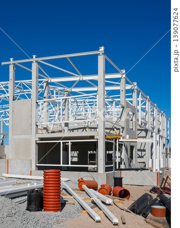 Concrete and steel frame building under construction with pipes and materials on sunny site 139077624