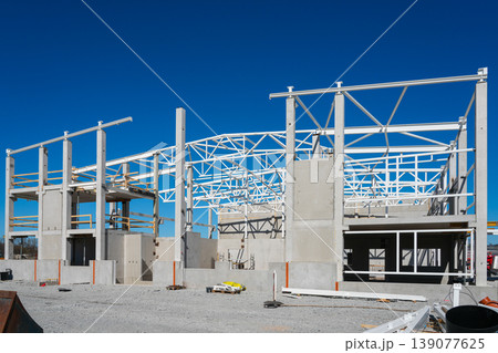Concrete columns and steel roof frame of industrial building under construction on clear blue sky Concrete columns and steel roof frame of industrial building under construction on clear blue sky 139077625