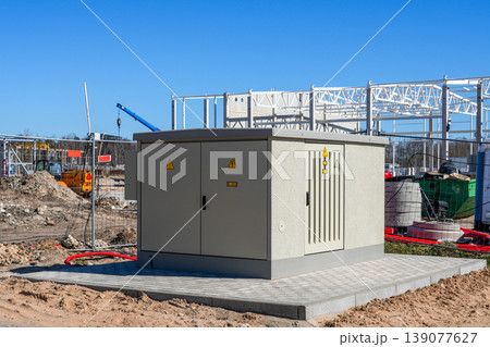Electrical transformer unit installed at construction site with industrial building in background 139077627