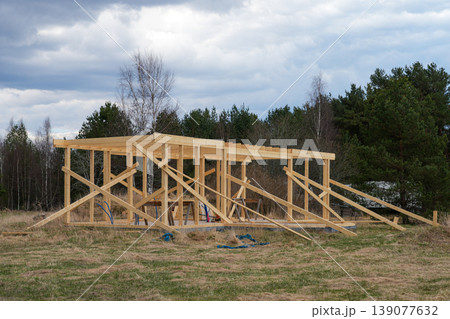 Wooden house frame under construction in rural landscape with timber structure and cloudy sky Wooden house frame under construction in rural landscape with timber structure and cloudy sky 139077632