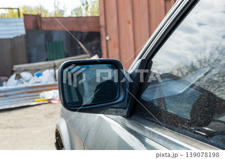 A car side mirror shows a reflection of the surroundings while parked in an industrial area with debris and structures nearby A car side mirror shows a reflection of the surroundings while parked in an industrial area with debris and structures nearby 139078198