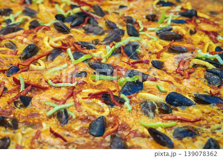 Seafood paella with mussels shrimp squid pepper rice cooked in large pan at street festival market closeup showing paella texture, ingredients. Street food culture, culinary tradition, outdoor cooking Seafood paella with mussels shrimp squid pepper rice cooked in large pan at street festival market closeup showing paella texture, ingredients. Street food culture, culinary tradition, outdoor cooking 139078362