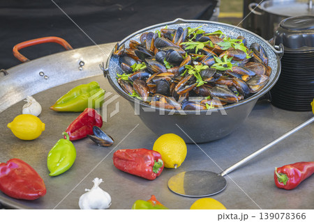 Mussels served in bowl with herbs on metal table with peppers, lemon, garlic. Mussels preparation, fresh ingredients closeup. Seafood cooking, mussels dish, gourmet seafood, fresh market cooking 139078366