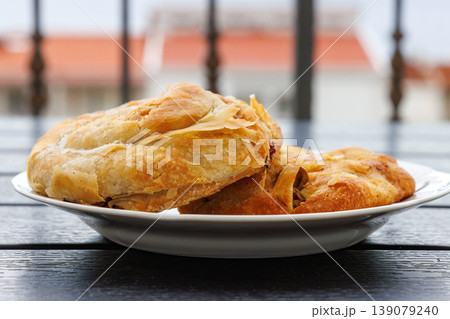 Side view of a white plate with sweet burek pastry roll and focaccia on a dark balcony table, with soft background. 139079240