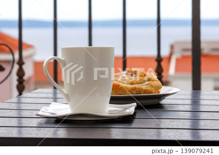 Side view of a white cup of tea and  plate with burek pastry on a balcony table with the view on  Adriatic sea in Makarska, Croatia on soft background. 139079241