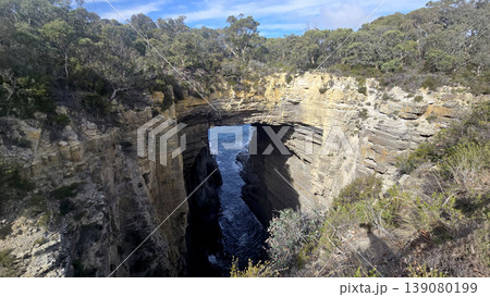 Dramatic natural rock archway carved by the ocean over deep blue sea waters 139080199