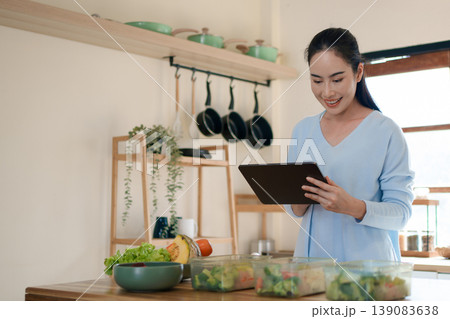 Woman using tablet to follow healthy cooking recipe while preparing fresh meal at home kitchen 139083638