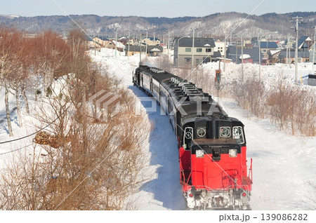 北海道の雪景色を走るSL列車とローカルな町並み 139086282