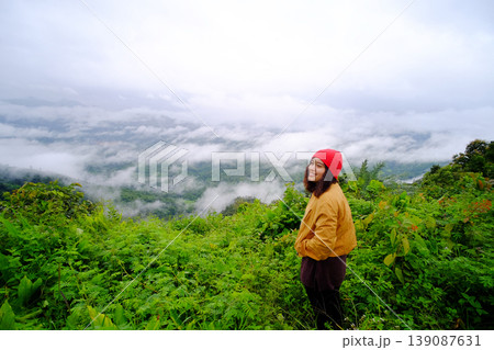 Tourist Asian young woman wearing red hat and yellow jacket standing on peak of mountains and mist in the morning of Thailand Tourist Asian young woman wearing red hat and yellow jacket standing on peak of mountains and mist in the morning of Thailand 139087631