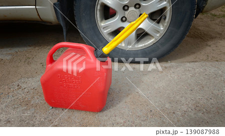 Gas can sits next to a car tire on a dirt surface in bright light 139087988