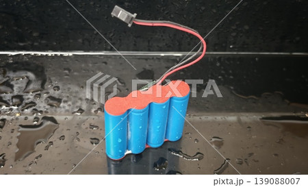 Battery pack with blue casing placed on a wet surface under bright light Battery pack with blue casing placed on a wet surface under bright light 139088007