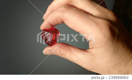 Hand holds a red heart-shaped gem in front of a dark background during daylight Hand holds a red heart-shaped gem in front of a dark background during daylight 139088062