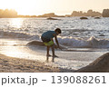 Child playing at shoreline with small waves during golden sunset light on sandy beach 139088261