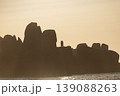 Rocky coastline silhouette at sunset with warm tones and calm sea creating peaceful horizon view 139088263
