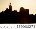 Lighthouse silhouette against golden sunset with rocky coastline creating dramatic scenic seascape composition 139088273