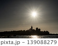 Sunset silhouette of lighthouse and rocky coastline with bright sun reflecting over calm sea 139088279