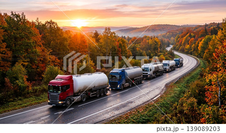 Trucks travel on winding road through forest as sun rises over autumn landscape in early morning hours 139089203
