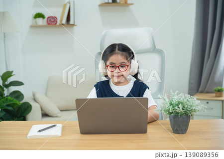 Young girl wearing headphones studying at home with laptop in modern living room, focused on learning and engaging in online education activities 139089356