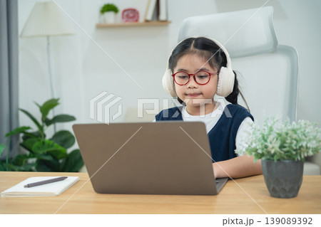 Young girl with headphones focused on laptop in modern home office, engaging in online learning or digital activities, educational technology concept 139089392