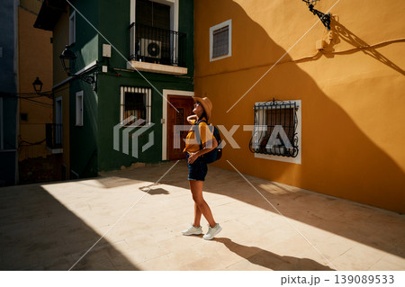 Woman traveler with backpack and straw hat looking at colorful buildings and houses Villajoyosa city in sunny day Woman traveler with backpack and straw hat looking at colorful buildings and houses Villajoyosa city in sunny day 139089533