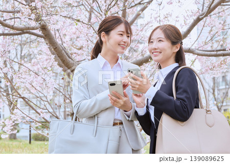 桜の下でスマートフォンを見ながら会話する新入社員の若い女性二人・春のビジネスシーン 139089625
