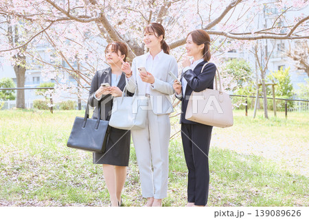 桜の下でスマホを持ちながら会話する3人の若手女性ビジネスパーソン・春の新生活イメージ 139089626