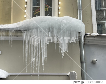 Icicles hanging from snow-covered roof of building against window 139090063