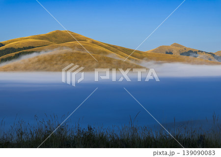 Fog rolling over golden hills of Castelluccio plateau Fog rolling over golden hills of Castelluccio plateau 139090083