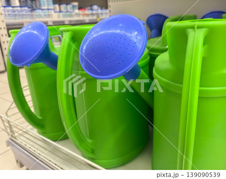 Bright green watering cans with blue nozzles displayed in a store aisle 139090539