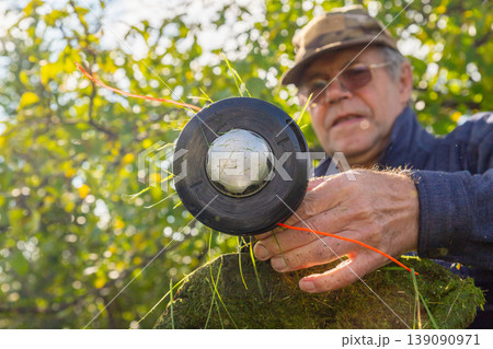 Man cleaning trimmer head of lawn mower. Gardener maintaining grass cutting equipment. Outdoor garden landscape care, maintenance service and seasonal landscaping tool repair concept. 139090971