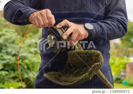 Man installing new trimmer line on a grass trimmer head. Garden maintenance and home improvement concept for outdoor work. close up view 139090972
