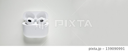 Wireless white earphones in a charging case on a light background. Minimalist composition of modern earbuds with large copy space for design. Technology and audio gadget concept 139090991