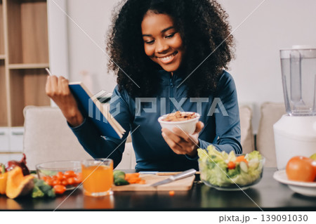 Young nutritionist showing bell peppers during an online video call consulting about healthy eating, sitting at home at a table with vegetables, laptop and measuring tape 139091030