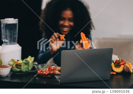 Young nutritionist showing bell peppers during an online video call consulting about healthy eating, sitting at home at a table with vegetables, laptop and measuring tape Young nutritionist showing bell peppers during an online video call consulting about healthy eating, sitting at home at a table with vegetables, laptop and measuring tape 139091036