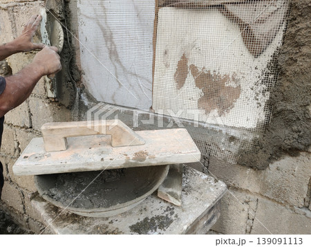 Mason applying cement plaster on wall mesh during home repair work Mason applying cement plaster on wall mesh during home repair work 139091113