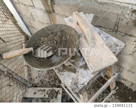 Plaster mixture waits in a round tray next to a wooden trowel tool 139091115
