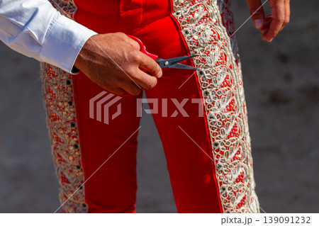 Close up detail of a bullfighter holding scissors next to his red traje de luces during a summer bullfight. Close up detail of a bullfighter holding scissors next to his red traje de luces during a summer bullfight. 139091232