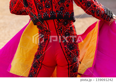 A bullfighter stands in the ring displaying his capote before engaging the bull. 139091242