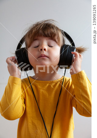 Portrait of a three year old girl with pigtails wearing yellow and listening to music with big headphones Portrait of a three year old girl with pigtails wearing yellow and listening to music with big headphones 139091265