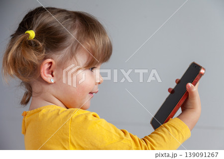 Toddler with pigtails using a mobile phone, concept of early digital exposure. 139091267