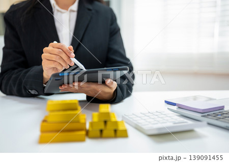 Gold investment concept with businesswoman analyzing market data on tablet, stack of gold bars. Gold investment concept with businesswoman analyzing market data on tablet, stack of gold bars. 139091455