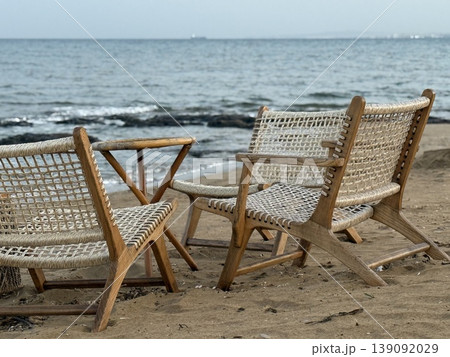 Beach scene with wooden chairs on sandy shore, ocean waves in the background, summer relaxation Beach scene with wooden chairs on sandy shore, ocean waves in the background, summer relaxation 139092029
