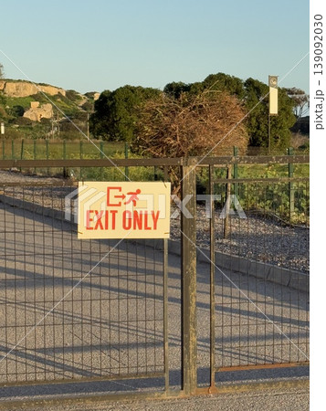 Exit only sign on metal gate in rural outdoor area with gravel path and trees Exit only sign on metal gate in rural outdoor area with gravel path and trees 139092030