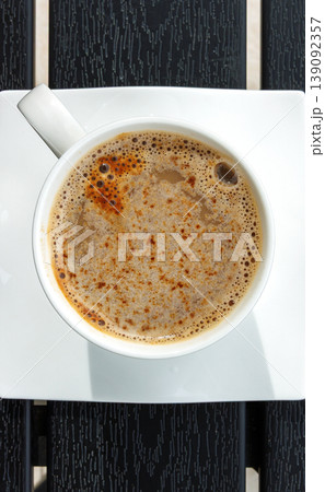 Cup of coffee on a square white saucer, placed on a dark slatted table. Selective focus. Copy space 139092357