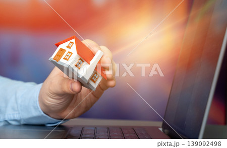 The concept of searching for housing via the Internet. Find an apartment for rent online. Property valuation and realtor services. House in hand with laptop. 139092498