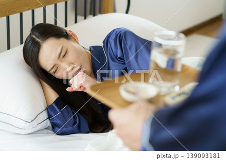 ベッドで咳き込む女性と薬を持ってくる男性の手 ベッドで咳き込む女性と薬を持ってくる男性の手 139093181